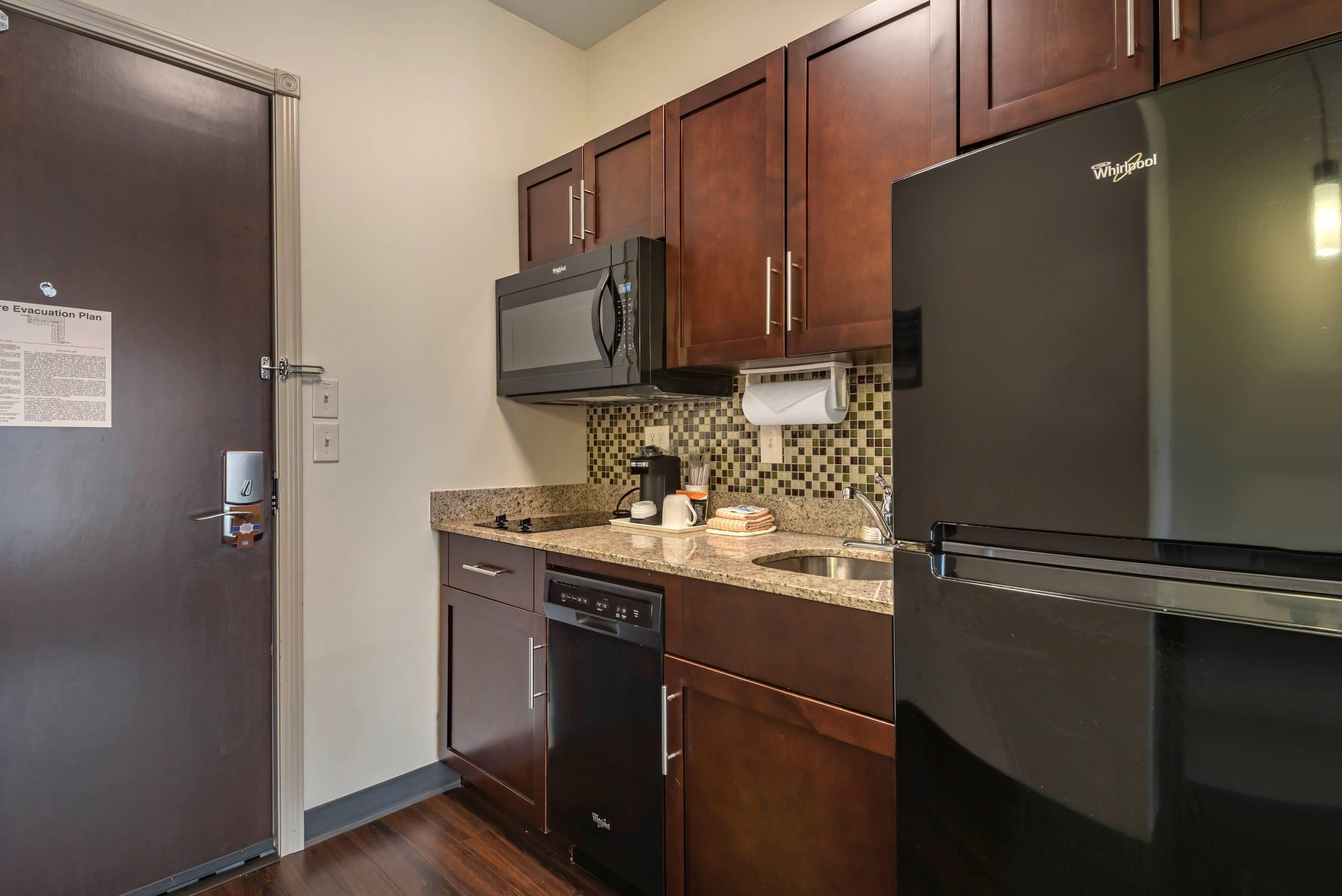 A compact kitchen with a microwave, refrigerator, dishwasher, and a tiled backsplash.