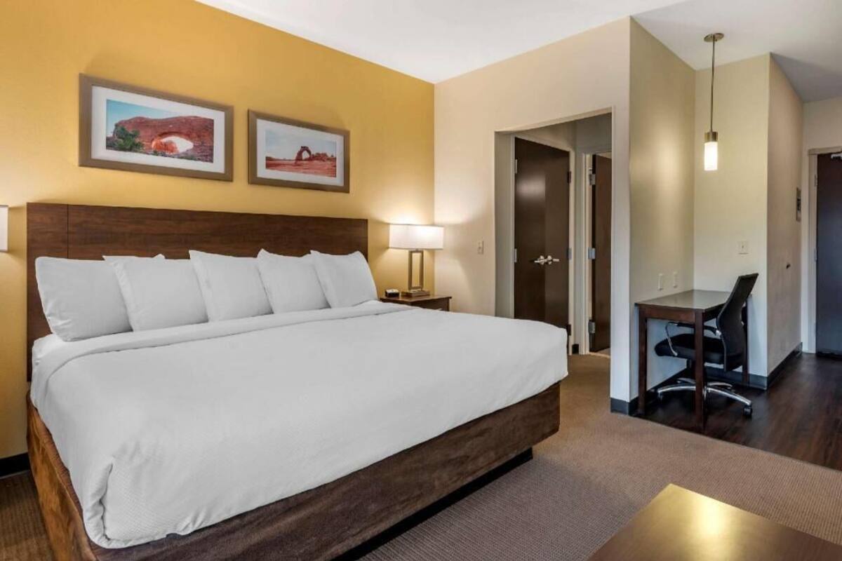 Una habitación de hotel con una cama grande, un escritorio y dos cuadros en la pared.