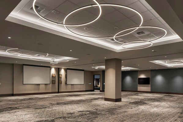 A spacious conference room with a patterned carpet, a large screen, and modern circular ceiling lights.