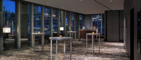 A modern hotel lobby with glass walls, multiple tables, and a bar area.