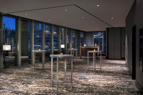 A modern hotel lobby with glass walls, multiple tables, and a bar area.