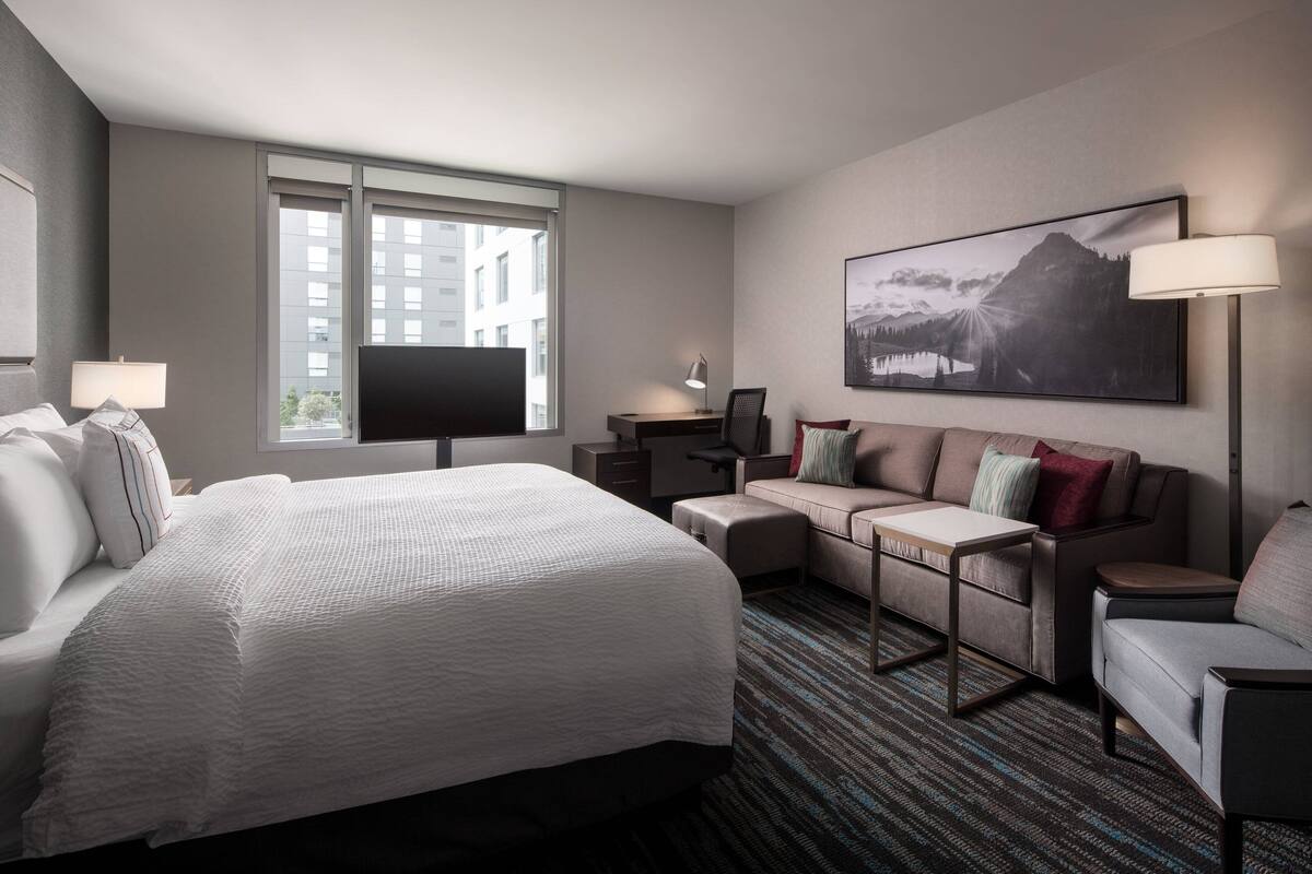 A hotel room with a large bed, a desk, a sofa, and a TV.