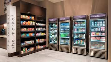 A hotel lobby with a self-service market area, including refrigerated beverage dispensers and shelves stocked with snacks and beverages.