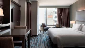 Une chambre d’hôtel équipée d’un lit, d’un bureau, d’une chaise, d’une télévision et offrant une vue sur le paysage urbain.