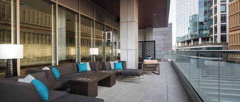 Un espacio lounge moderno al aire libre con sofás, mesas y lámparas, con vistas a un paisaje urbano.