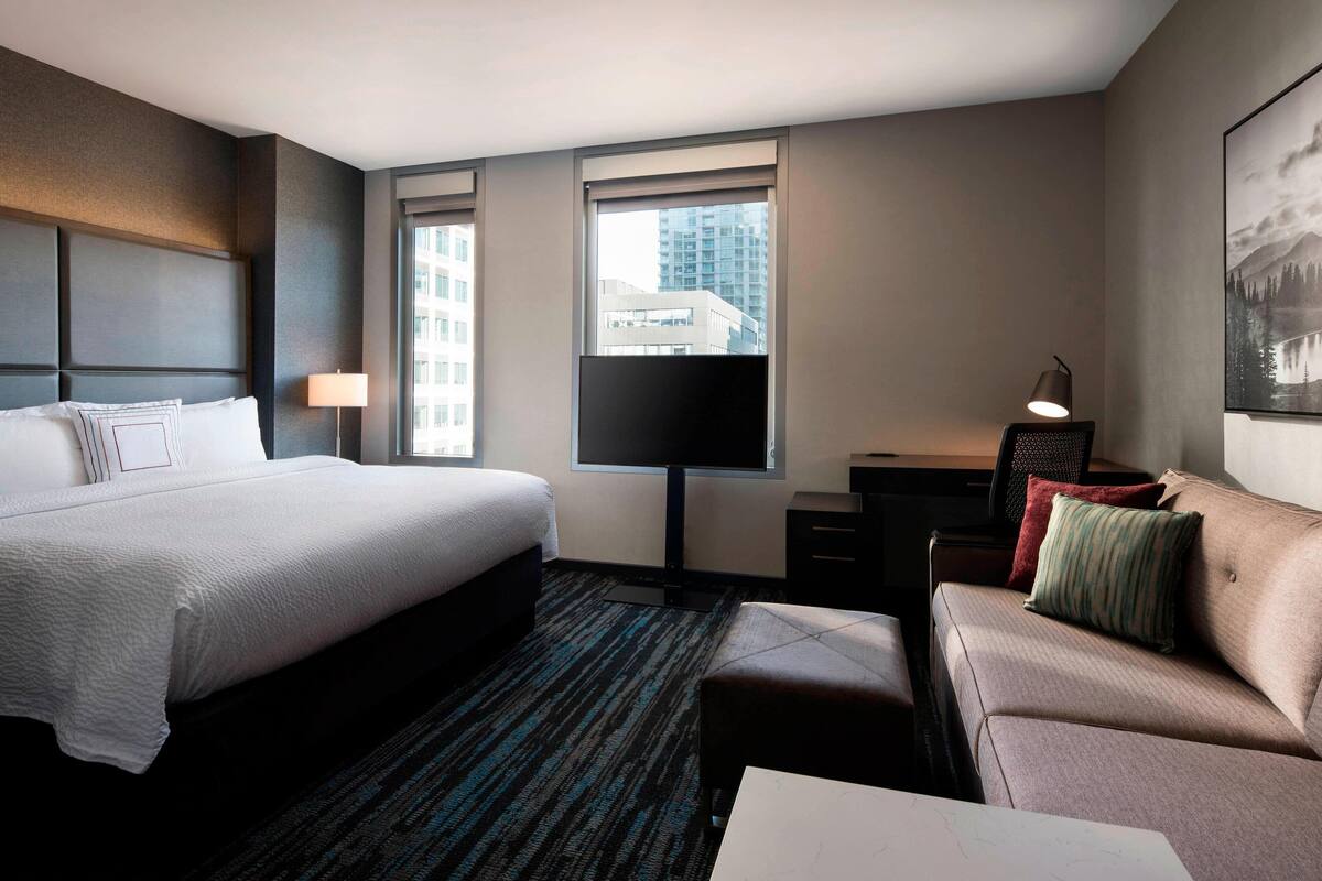 A hotel room with a large bed, a sofa, a desk, and a TV.