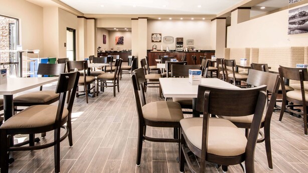 A spacious hotel dining area with multiple tables and chairs, a reception desk, and a view of the cityscape through large windows. - Sleep Inn & Suites Moab near Arches National Park (Moab)