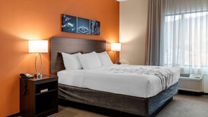 A hotel room with a bed, two bedside lamps, a nightstand with a phone, a wall art piece, and a window with curtains. - Sleep Inn & Suites Moab near Arches National Park (Moab)