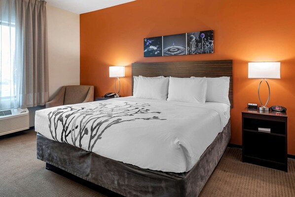 A hotel room with a large bed, two bedside tables with lamps, a chair, and a wall-mounted artwork.