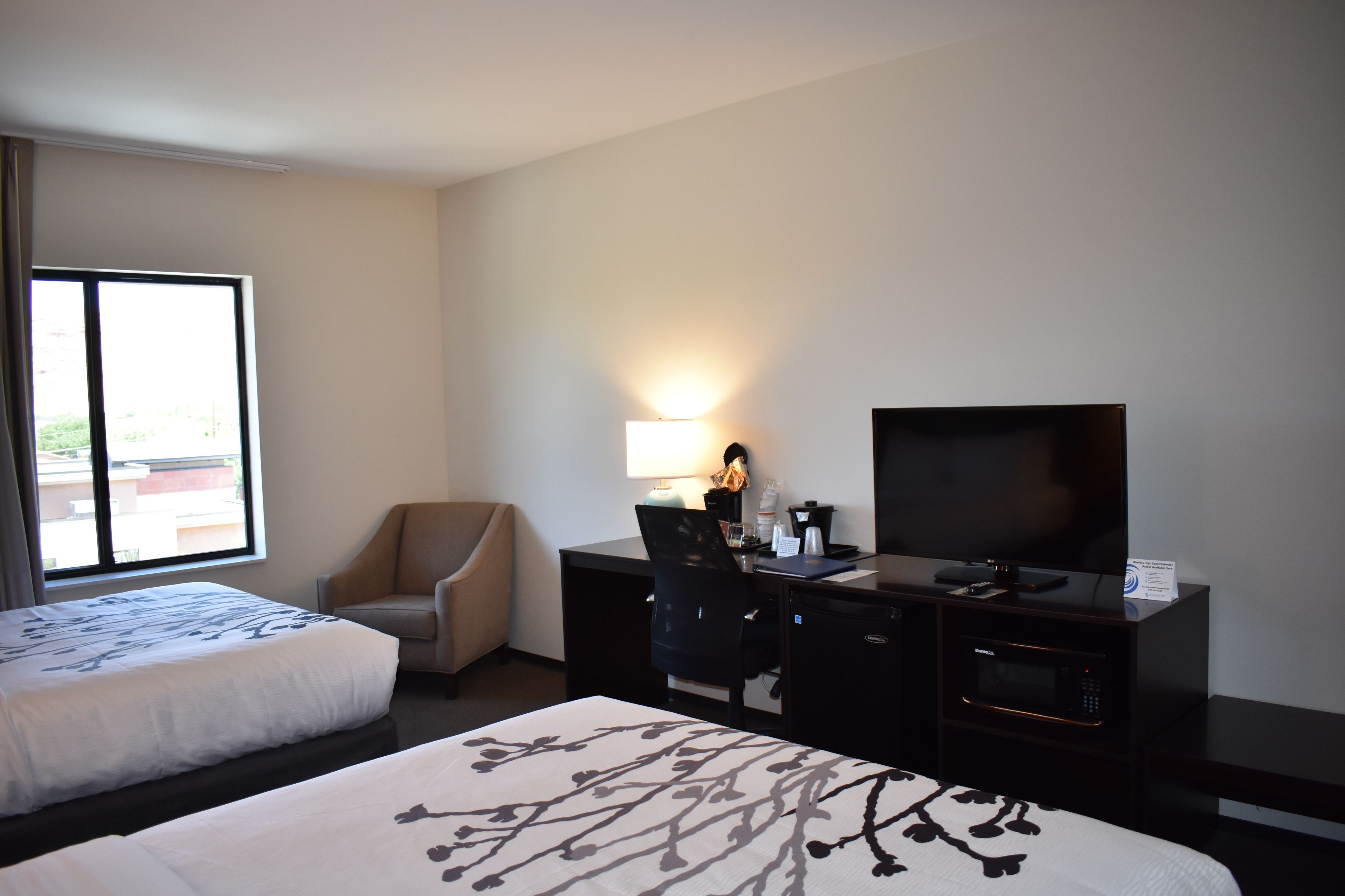 A hotel room with two beds, a desk with a television, a chair, and a desk lamp.