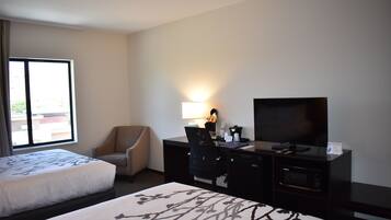 A hotel room with two beds, a desk with a television, a chair, and a desk lamp.