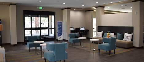 A hotel lobby with a reception desk, seating area with sofas and chairs, a piano, and a large window.