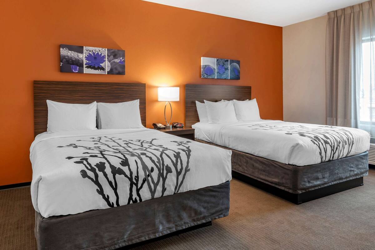 A hotel room with two beds, a nightstand with a lamp, and artwork on the walls.