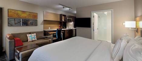 Habitación de hotel con una cama grande, un sofá, un escritorio, un microondas, un televisor de pantalla plana y una puerta corredera al baño.