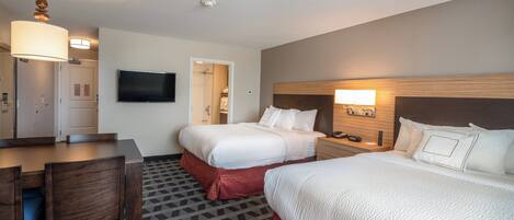 Une chambre d’hôtel avec deux lits, un bureau, une chaise, un téléviseur fixé au mur et un espace douche visible à travers une porte ouverte.