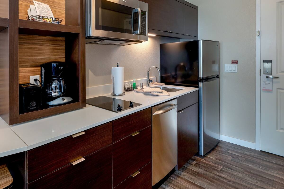 A modern kitchen with a stainless steel refrigerator, a built-in microwave, and a coffee maker.