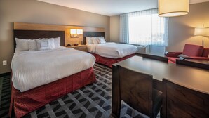 Habitación de hotel con dos camas, un escritorio, una silla y un ventanal con cortinas.