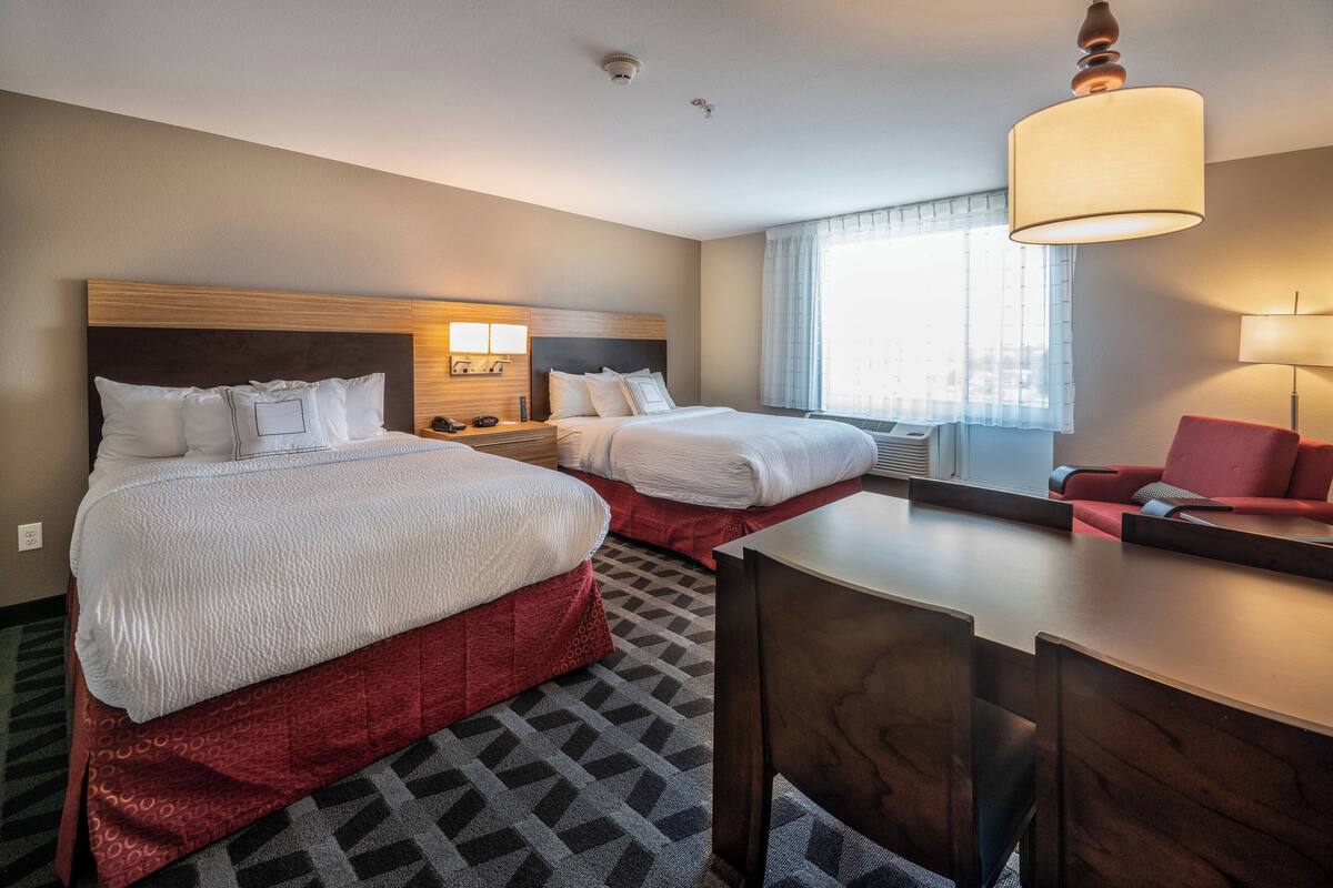 A hotel room with two beds, a desk, a chair, and a window with curtains.