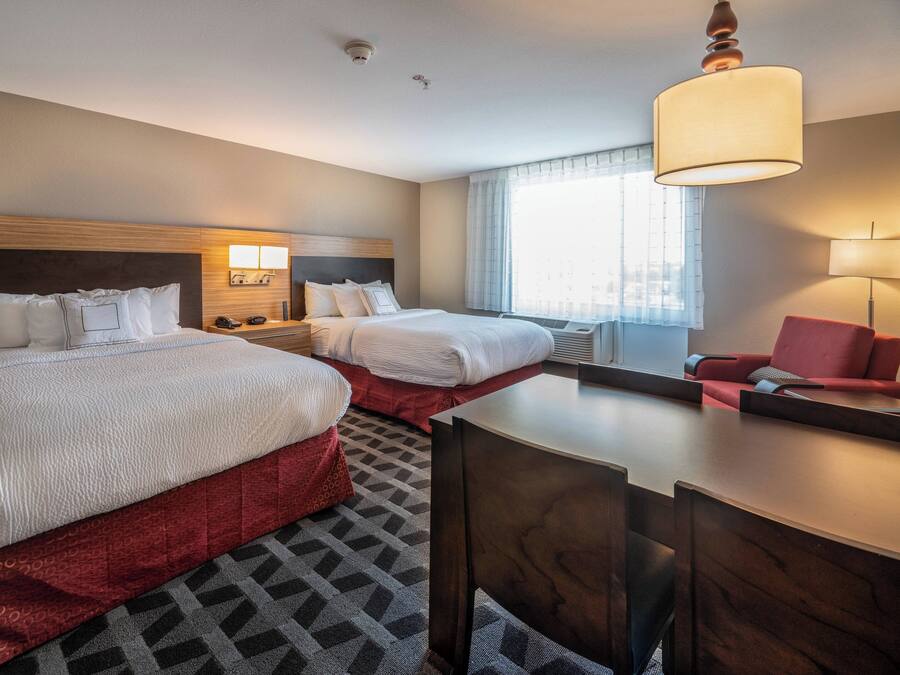 A hotel room with two beds, a desk, a chair, and a window with curtains.