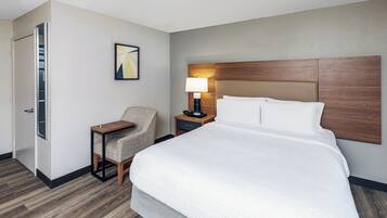A hotel room with a large bed, a chair, a nightstand with a lamp, and a door leading to a closet.