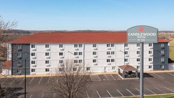 A hotel with a large parking lot, a covered outdoor seating area, and a sign indicating it is Candlewood Suites by IHG.