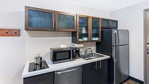 A modern kitchen with dark cabinets, a stainless steel refrigerator, a microwave, and a dishwasher. - Candlewood Suites Topeka West by IHG (Topeka)
