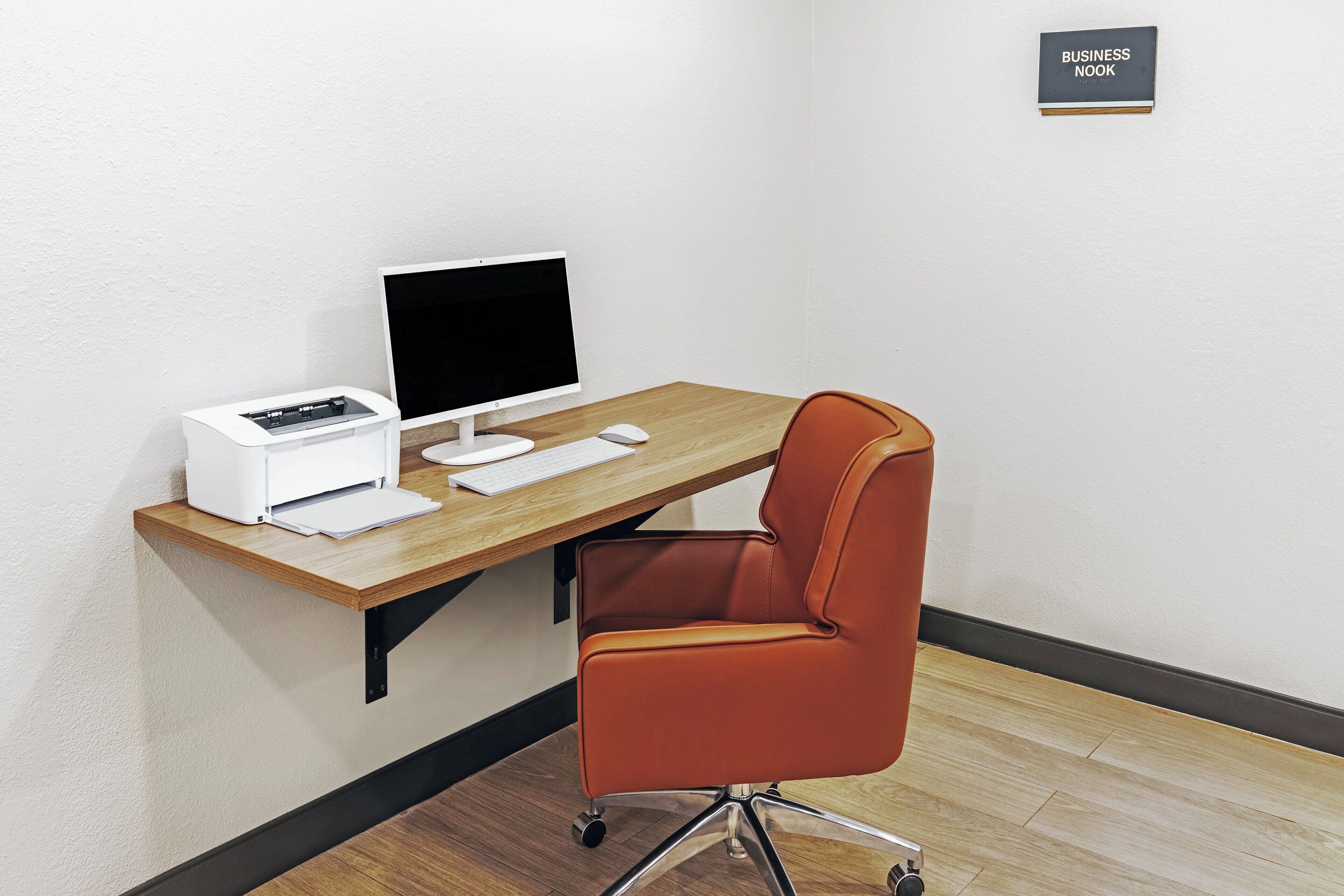 A workspace with a computer, printer, keyboard, and mouse on a wooden desk against a white wall.