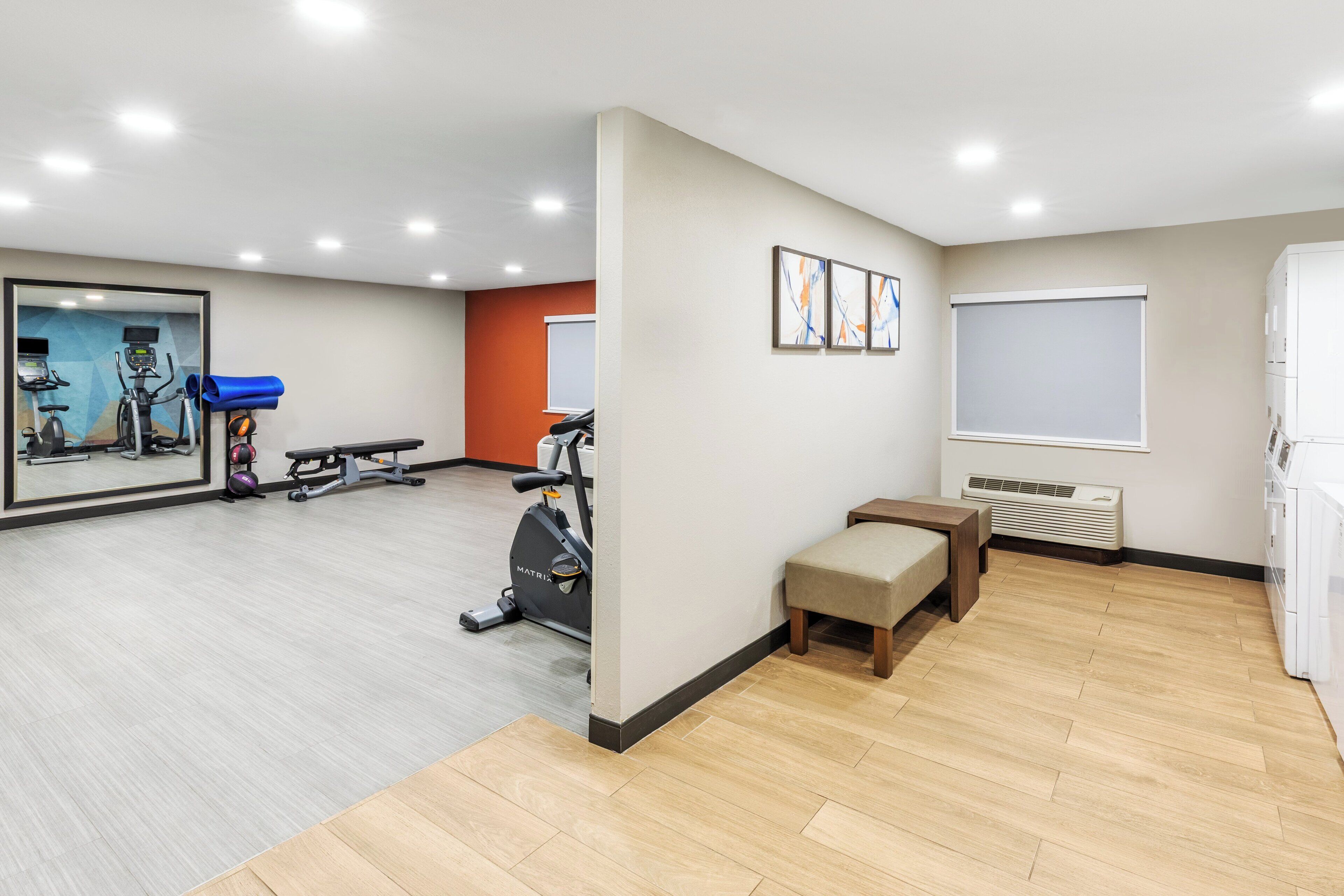 A spacious room with a large mirror, exercise equipment, a bench, and a window.