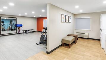 A spacious room with a large mirror, exercise equipment, a bench, and a window.