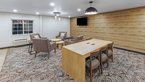 A conference room with a wooden table, chairs, a small round table, and a TV mounted on the wall.