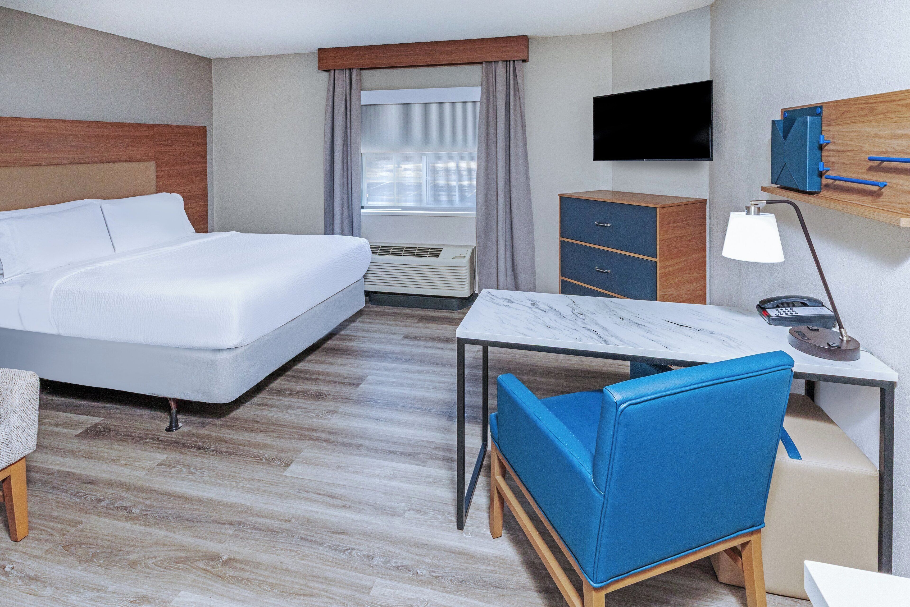 A hotel room with a bed, desk, chair, TV, and a dresser.
