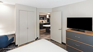 A hotel room with a bed, a desk, a TV, and a view into the kitchen area.