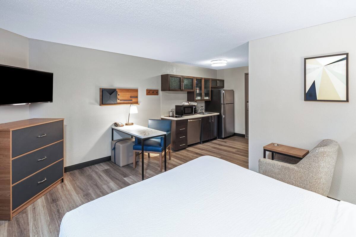Une chambre d’hôtel équipée d’un lit, d’un bureau, d’une chaise, d’une kitchenette et d’un téléviseur.