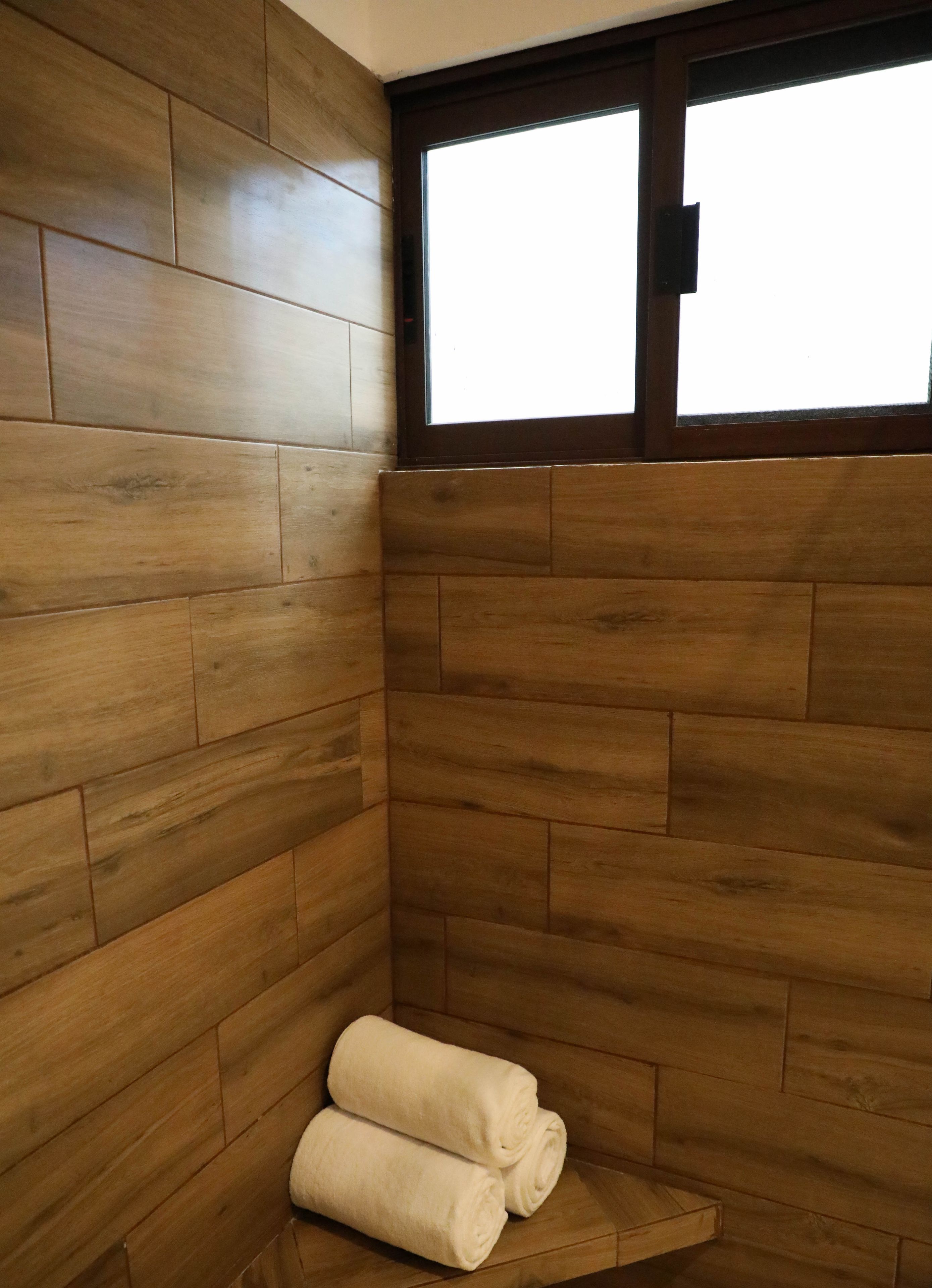 A corner of a room with wooden paneling and a window. There are two rolled towels on the floor.