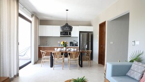 A modern kitchen with white cabinets, a dining table with chairs, a coffee machine, and a refrigerator. - Alquimia 2 bedroom apartment sleeps 4 (Tulum)