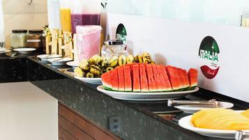 A breakfast buffet with various fruits, a watermelon, and a juice dispenser.