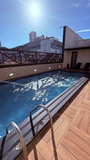 Ein Dachpool mit Metallleiter, umgeben von einer Holzterrasse und einer Ziegelwand.