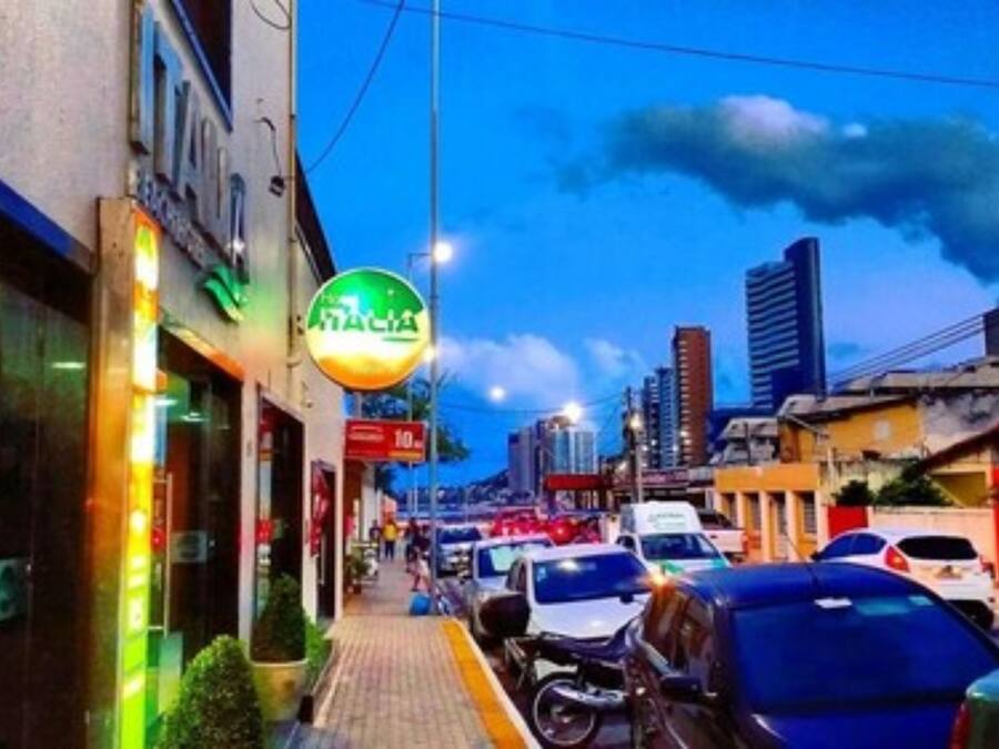 Una vista urbana amb cotxes aparcats, vorada i edificis amb cartells.