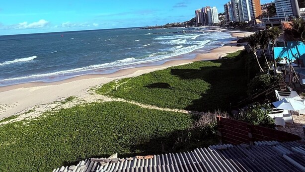 A beach view with high-rise buildings in the background, a clear sky, and a wooden deck in the foreground. - Hotel Italia Beach (Natal)