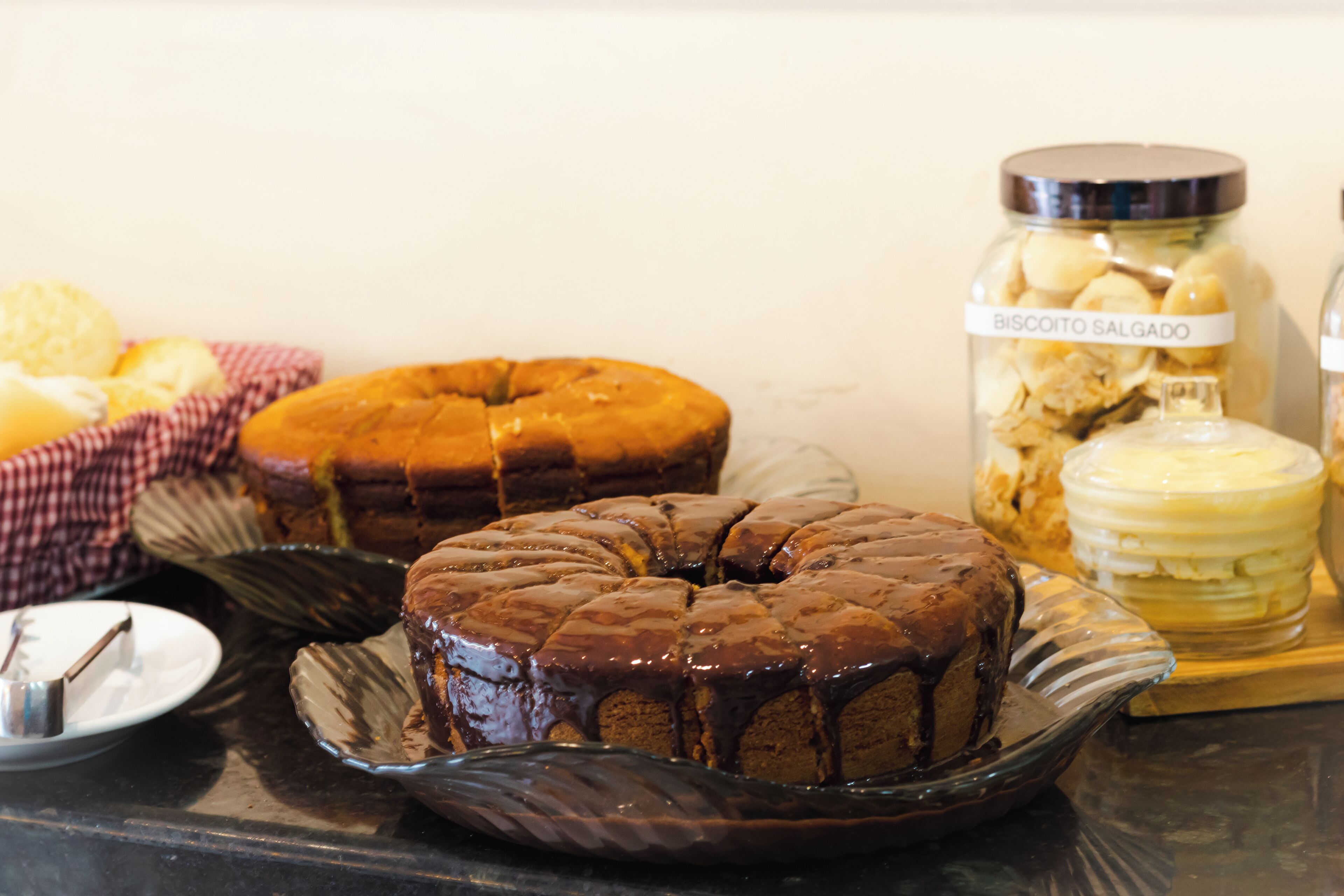 Un gâteau au chocolat en forme de couronne, présenté sur une assiette en verre, un bocal de biscuits secs et un bocal de glaçage au beurre.