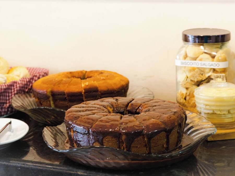 Un gâteau au chocolat en forme de couronne, présenté sur une assiette en verre, un bocal de biscuits secs et un bocal de glaçage au beurre.