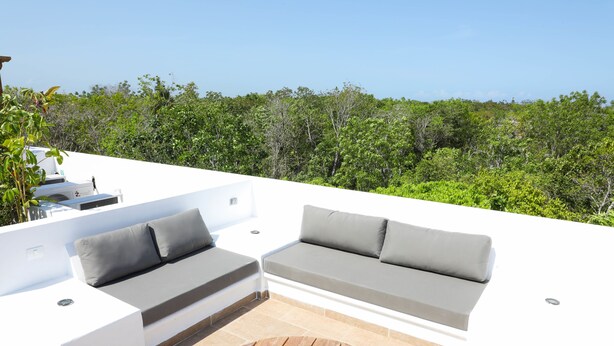 A modern outdoor seating area with a white wall, grey cushions, and a wooden table. - Tony Condo 2 bedroom sleeps 4 (Tulum)