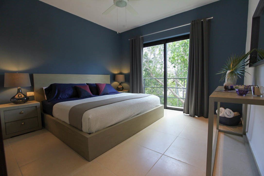 Un dormitorio con cama, mesitas de noche, una mesa con una planta y una ventana con cortinas.