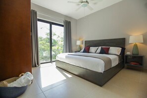 Un dormitorio de hotel moderno con una cama grande, ventilador de techo y vista a través de la puerta de vidrio.
