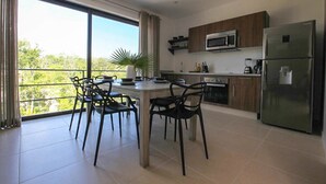 A modern kitchen with a dining area, large windows, and a view of greenery. - Martiki Condo 2 bedroom sleeps 4 (Tulum)