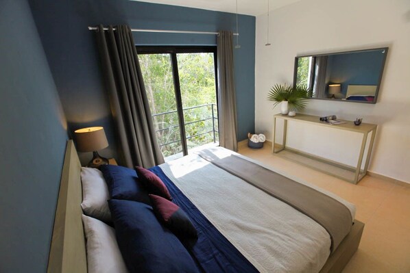 Un dormitorio moderno con una cama grande, una mesita de noche, un espejo y vistas al verde exterior.