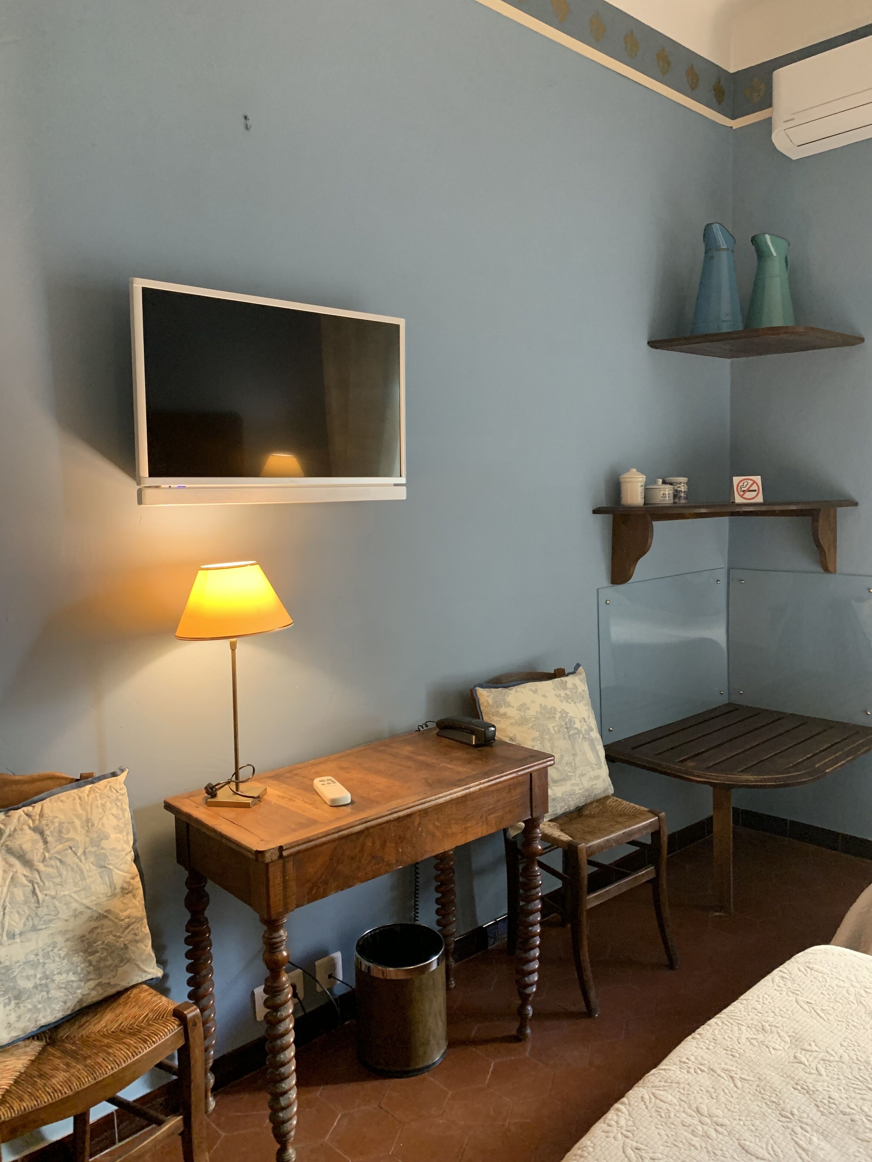 Habitación de hotel con escritorio de madera, lámpara, silla, cama, televisor y cubo de basura.