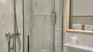 Ein modernes Badezimmer mit einer gläsernen Duschkabine, einem weißen Waschbecken und einem Spiegel mit goldener Rahmung.