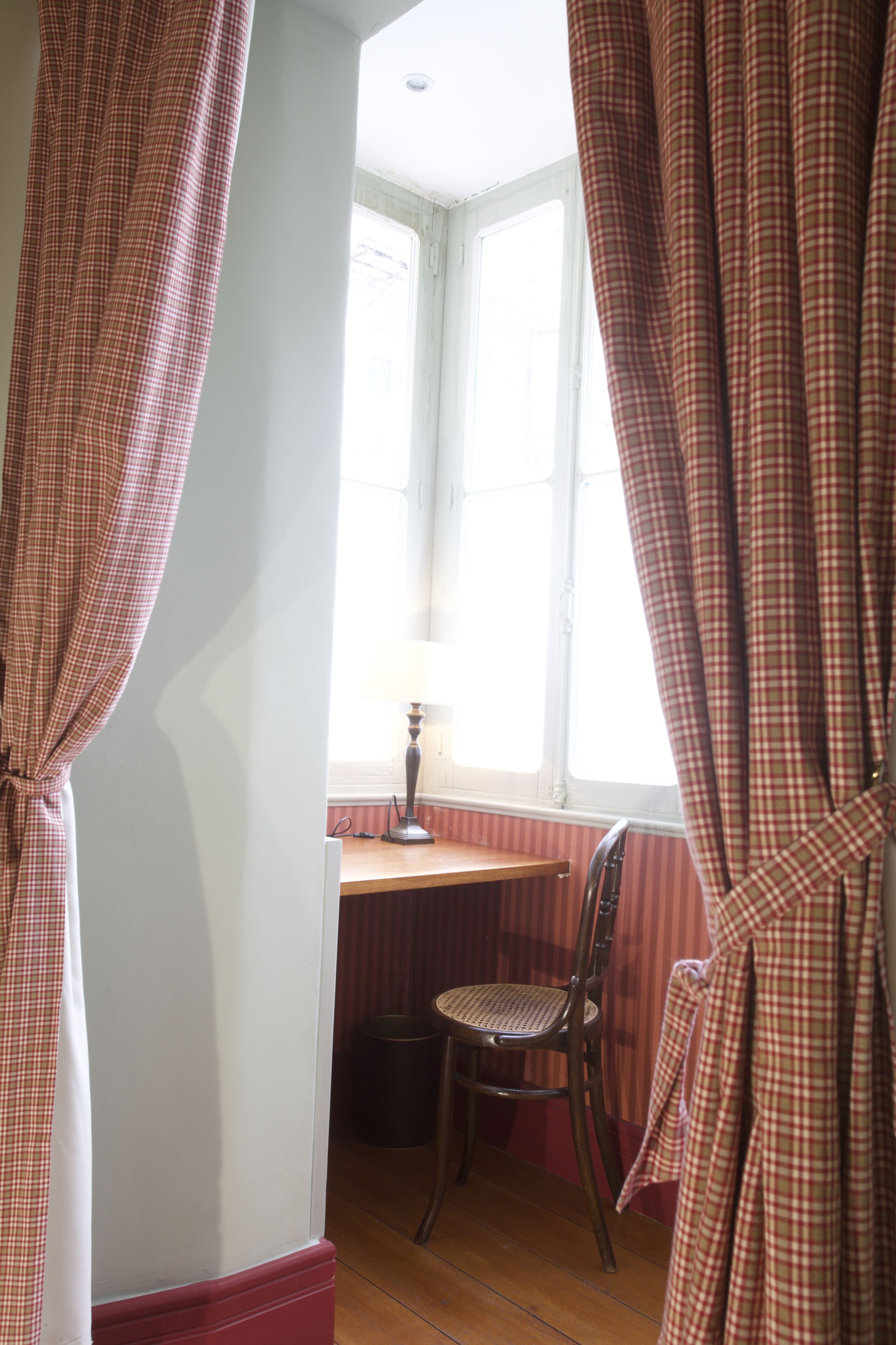 Una habitación con ventana, una silla, una lámpara y cortinas.
