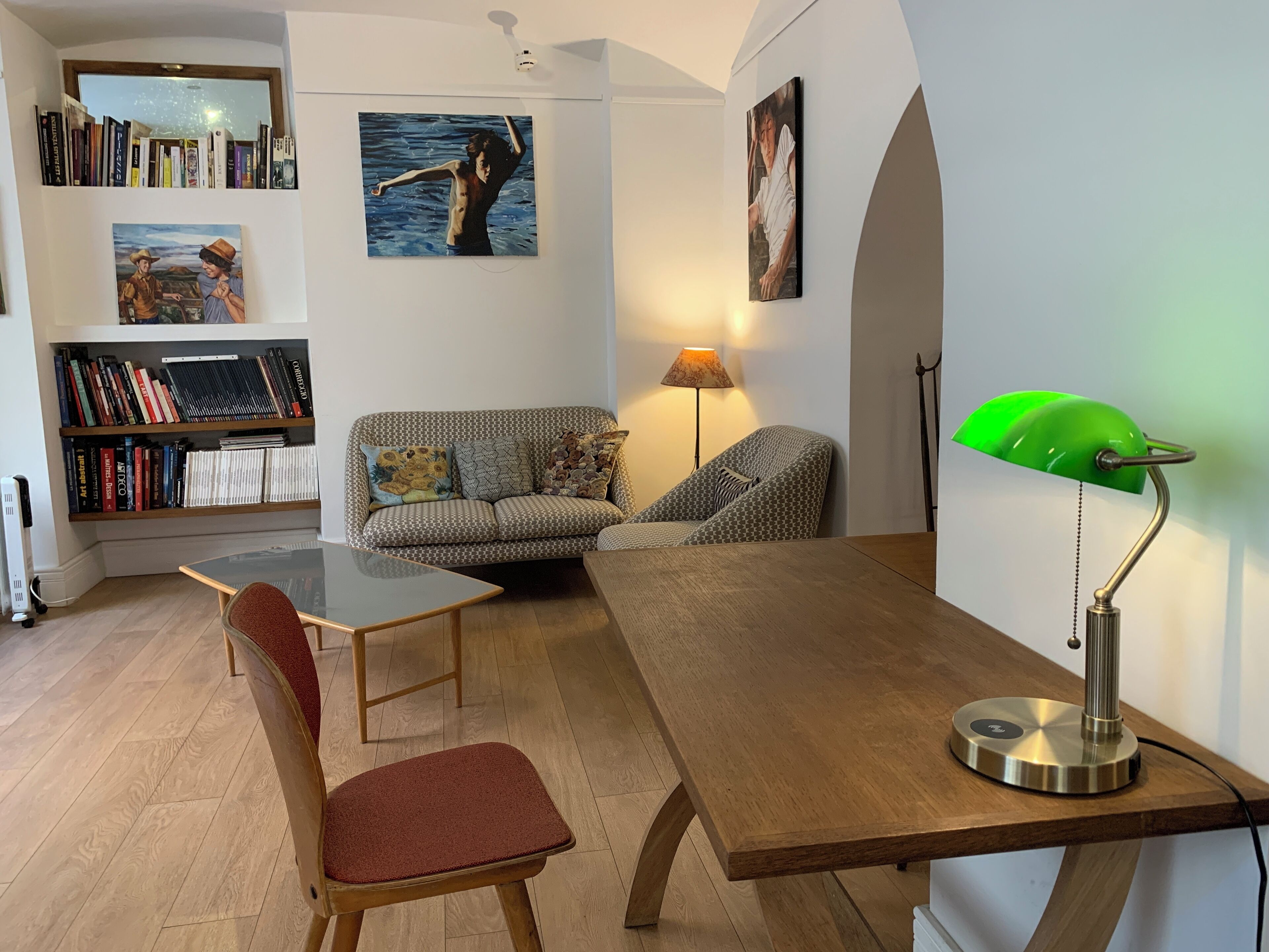 Una sala de estar moderna con una mesa de madera, un sillón rojo, un sofá estampado y una estantería llena de libros.